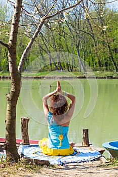 Young woman practice yoga outdoor by the lake healthy lifestyle concept back view full body shot