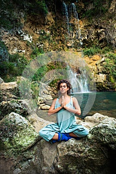 Young woman practice yoga outdoor on the rocks by the waterfall