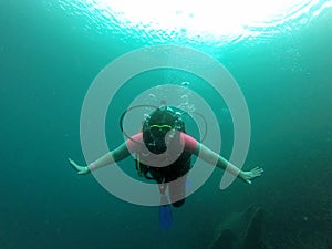 Young woman practices the sport scuba diving with oxygen tank equipment, visor, fins, relaxes and enjoys the bottom of the crystal