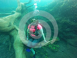 Young woman practices the sport scuba diving with oxygen tank equipment, visor, fins, relaxes and enjoys the bottom of the crystal