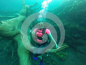 Young woman practices the sport scuba diving with oxygen tank equipment, visor, fins, relaxes and enjoys the bottom of the crystal