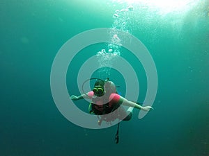 Young woman practices the sport scuba diving with oxygen tank equipment, visor, fins, relaxes and enjoys the bottom of the crystal