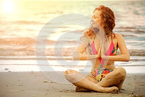 Young woman practices yoga on the beach in summer.