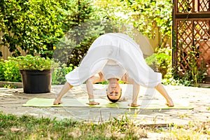 Young woman practices yoga in the garden. Prasarita Padottanasana or Wide Stance Forward Bend