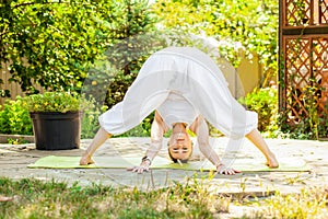 Young woman practices yoga in the garden. Prasarita Padottanasana or Wide Stance Forward Bend