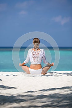 Young woman practices yoga and meditates in the lotus position on the beach
