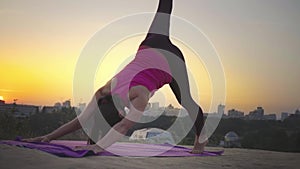 A young woman practices yoga on a mountain in the background of a big city