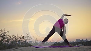 A young woman practices yoga on a mountain in the background of a big city