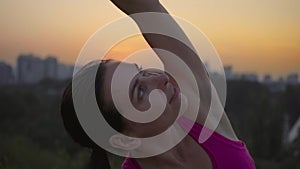 A young woman practices yoga on a mountain in the background of a big city