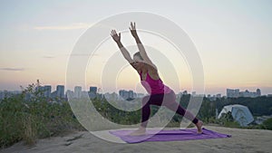 A young woman practices yoga on a mountain in the background of a big city