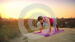 A young woman practices yoga on a mountain in the background of a big city. Healthy woman doing sports at sunset. A