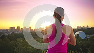 A young woman practices yoga on a mountain in the background of a big city. Healthy woman doing sports at sunset. A