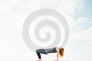 Young woman practices yoga outside. Blonde girl do upside down pose. Purvottanasana yoga posture. She dressed in black