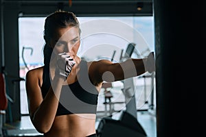 Young woman practicing boxing at the gym, she wears boxing gloves and hits a punching bag