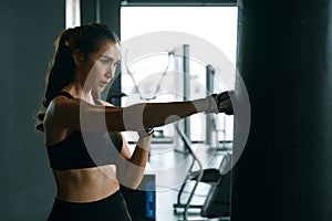 Young woman practicing boxing at the gym, she wears boxing gloves and hits a punching bag