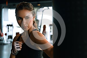 Young woman practicing boxing at the gym, she wears boxing gloves and hits a punching bag