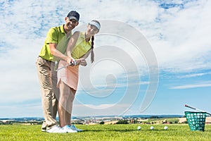 Young woman practicing the correct move during golf class with a skilled player