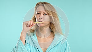 Young woman practicing dental hygiene, brushing teeth in a light blue robe