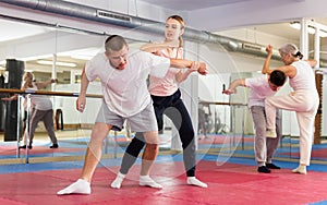 Young woman practicing elbow blow with wristlock to opponent in gym