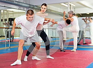 Young woman practicing elbow blow with wristlock to opponent in gym