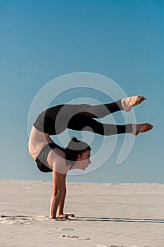 Young woman practicing handstand on beach with white sand and bright blue sky