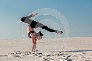 Young woman practicing handstand on beach with white sand and bright blue sky