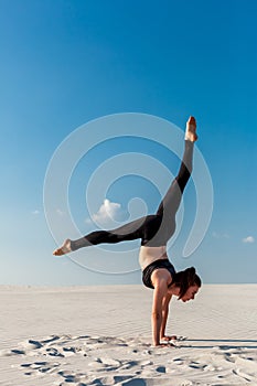 Young woman practicing handstand on beach with white sand and bright blue sky