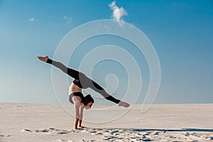 Young woman practicing handstand on beach with white sand and bright blue sky