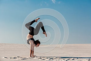 Young woman practicing handstand on beach with white sand and bright blue sky