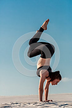 Young woman practicing handstand on beach with white sand and bright blue sky