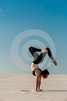 Young woman practicing handstand on beach with white sand and bright blue sky