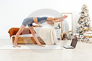 Young woman practicing at home bending forward with her arms outstretched.