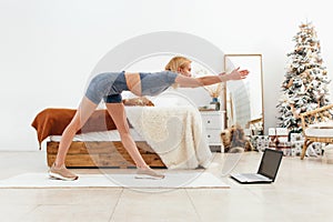 Young woman practicing at home bending forward with her arms outstretched.