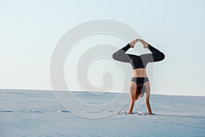 Young woman practicing inversion balancing yoga pose handstand on sand.