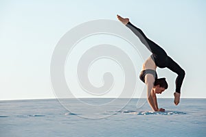 Young woman practicing inversion balancing yoga pose handstand on sand.