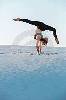 Young woman practicing inversion balancing yoga pose handstand on sand.