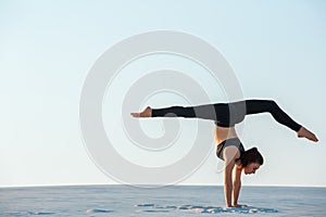 Young woman practicing inversion balancing yoga pose handstand on sand.