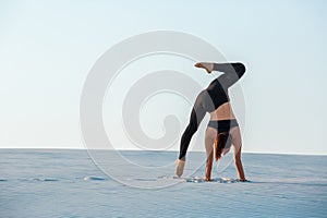 Young woman practicing inversion balancing yoga pose handstand on sand.