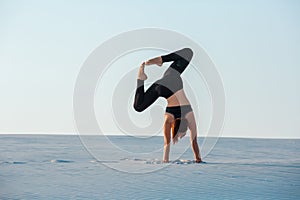 Young woman practicing inversion balancing yoga pose handstand on sand.