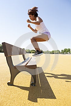 Young woman practicing jumping exercises on an outdoor bench