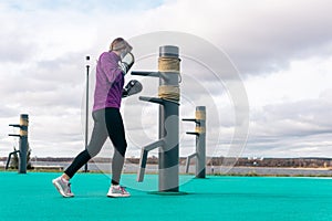 Young woman practicing martial arts alone on the sports ground with traditional dummies