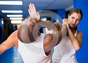 Young woman practicing palm heel strike to man in self-defense training in gym