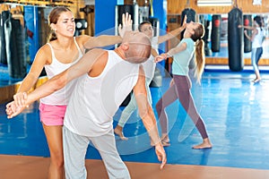 Young woman practicing palm heel strike to man in self-defense training in gym