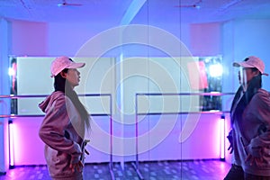 Young woman practicing performance dance in front of a large mirror at studio with neon light