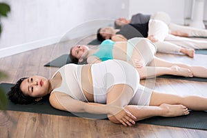 Young woman practicing revolved abdomen pose of yoga in light fitness room