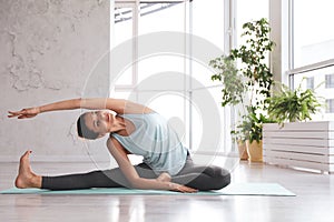 Young woman practicing revolved head to knee asana in studio. Parivrtta Janu Sirsasana pose