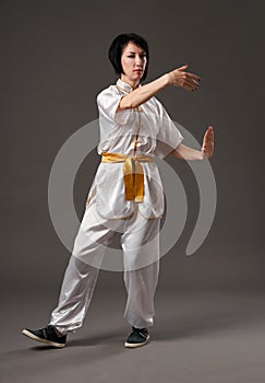 Young woman practicing tai chi chuan. Chinese management skill Qi`s energy. Gray background, studio shoot.