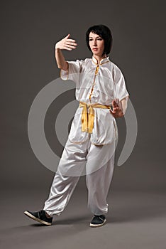 Young woman practicing tai chi chuan. Chinese management skill Qi`s energy. Gray background, studio shoot.