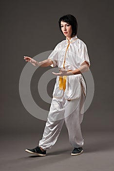 Young woman practicing tai chi chuan. Chinese management skill Qi`s energy. Gray background, studio shoot.