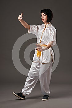 Young woman practicing tai chi chuan. Chinese management skill Qi`s energy. Gray background, studio shoot.